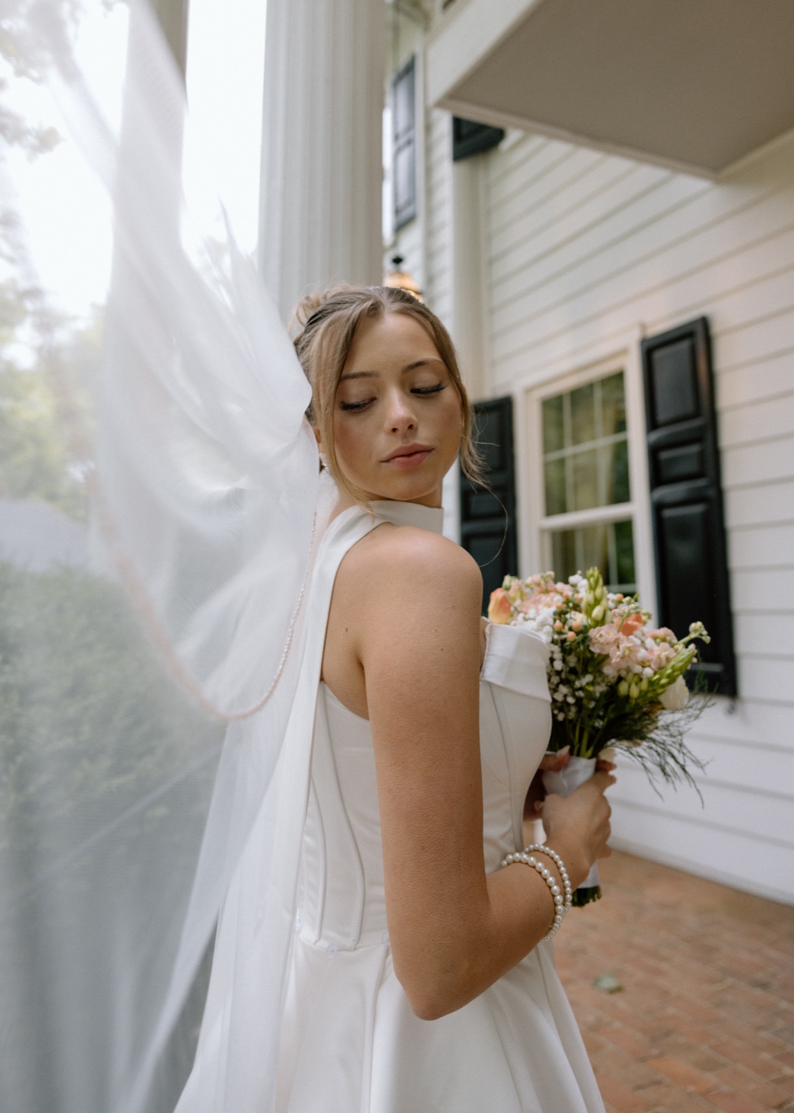 Bride outdoors with a flowing veil and bouquet, wearing soft natural makeup