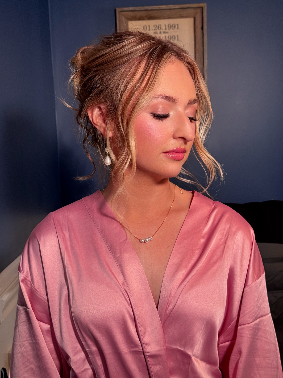 Blonde bride in a pink robe with a soft updo and rosy makeup